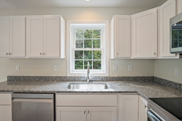 kitchen featuring dark stone counters, appliances with stainless steel finishes, sink, and white cabinets