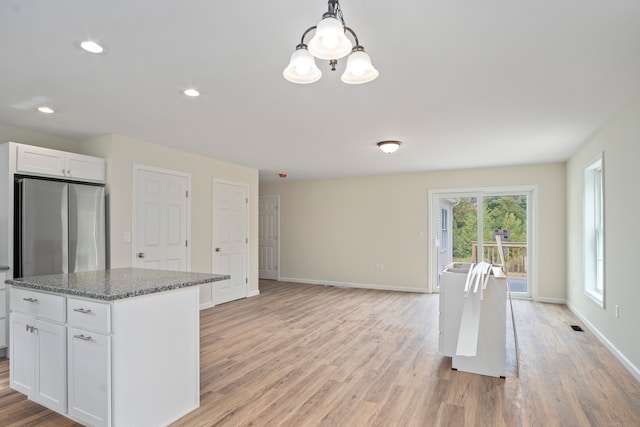 kitchen featuring white cabinets, hanging light fixtures, dark stone countertops, and light hardwood / wood-style flooring