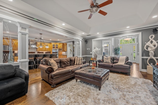 living room with ornate columns, dark hardwood / wood-style floors, ornamental molding, ceiling fan, and a tray ceiling