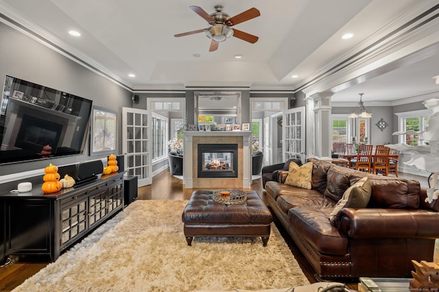 living room featuring dark wood-type flooring, ornate columns, crown molding, a tray ceiling, and a tile fireplace