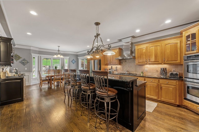 kitchen featuring wall chimney range hood, a breakfast bar area, appliances with stainless steel finishes, a center island, and decorative light fixtures