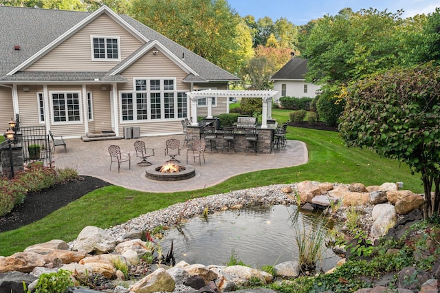 rear view of property featuring a lawn, a pergola, an outdoor bar, a fire pit, and a patio