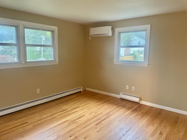 spare room with a healthy amount of sunlight, light hardwood / wood-style floors, baseboard heating, and a wall unit AC