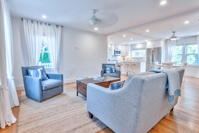 living room featuring ceiling fan, sink, and light wood-type flooring