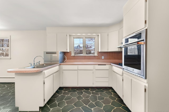 kitchen with white cabinets, tasteful backsplash, sink, kitchen peninsula, and stainless steel oven