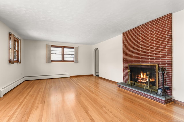 unfurnished living room featuring a brick fireplace, wood-type flooring, a baseboard heating unit, and a textured ceiling