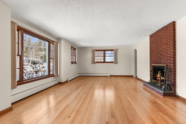 unfurnished living room with a textured ceiling, baseboard heating, light hardwood / wood-style floors, and a brick fireplace