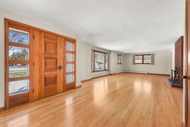 unfurnished living room featuring light wood-type flooring, a fireplace, and a baseboard heating unit