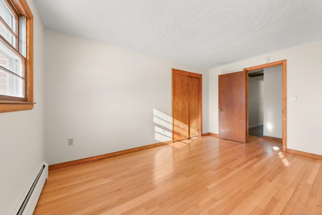 unfurnished bedroom with light wood-type flooring, a baseboard heating unit, a closet, and multiple windows