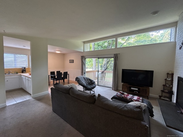 living room featuring a brick fireplace, light colored carpet, a healthy amount of sunlight, and sink