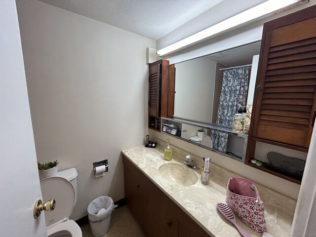 bathroom with a textured ceiling, vanity, and toilet