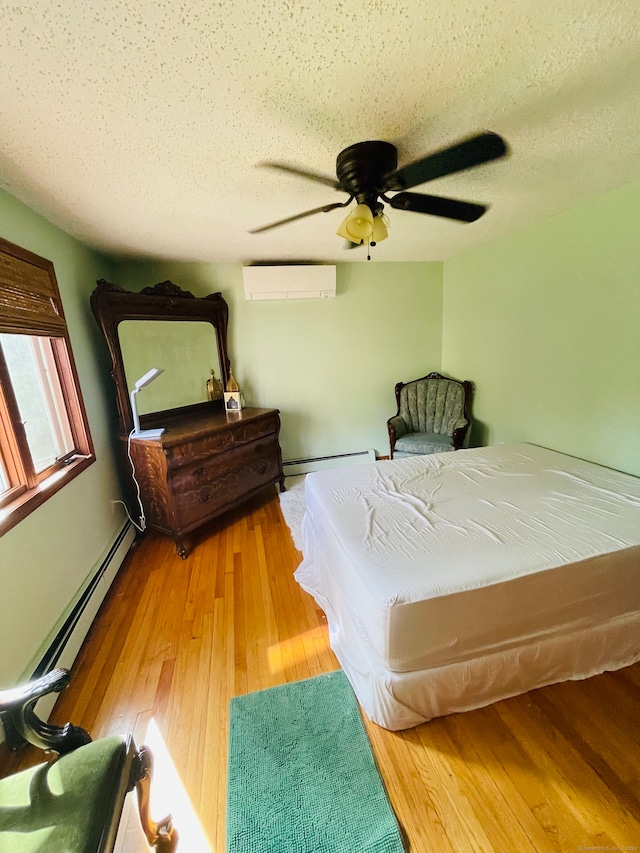 bedroom featuring a textured ceiling, hardwood / wood-style flooring, baseboard heating, a wall mounted air conditioner, and ceiling fan