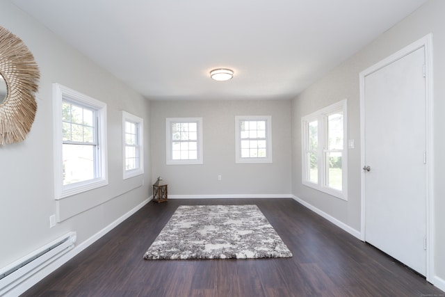 unfurnished room with dark hardwood / wood-style floors, a baseboard heating unit, and a wealth of natural light