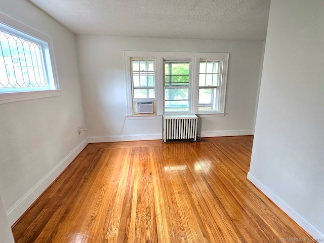 unfurnished room with light wood-type flooring, cooling unit, a textured ceiling, and radiator heating unit