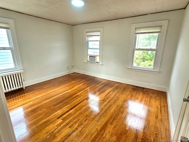 spare room with wood-type flooring, cooling unit, plenty of natural light, and radiator heating unit