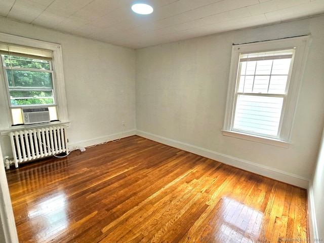 unfurnished room with radiator, a wealth of natural light, hardwood / wood-style flooring, and cooling unit