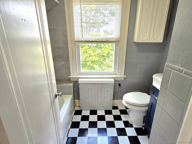 bathroom featuring tile walls, a tub to relax in, and toilet