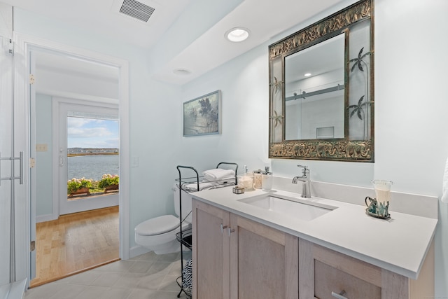 bathroom with vanity, hardwood / wood-style flooring, a water view, toilet, and a shower with door