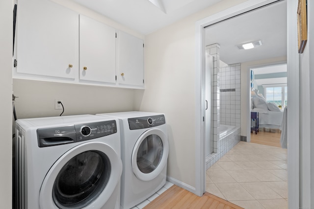 laundry room featuring washing machine and dryer, light tile patterned floors, and cabinets