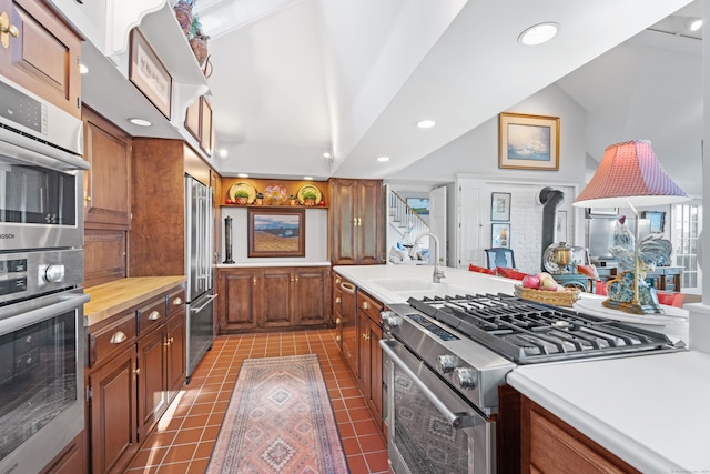 kitchen featuring dark tile patterned flooring, a wood stove, lofted ceiling, high quality appliances, and sink