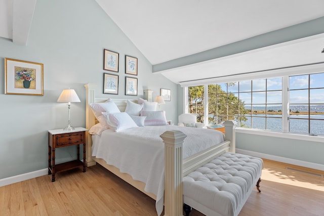 bedroom with light hardwood / wood-style floors, a water view, and vaulted ceiling