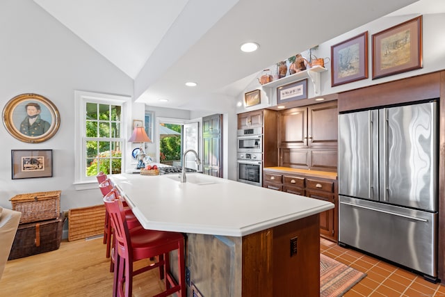 kitchen with a kitchen island with sink, sink, vaulted ceiling, a kitchen bar, and appliances with stainless steel finishes