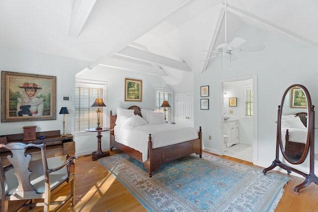 bedroom featuring vaulted ceiling with beams, light hardwood / wood-style floors, ensuite bathroom, and ceiling fan