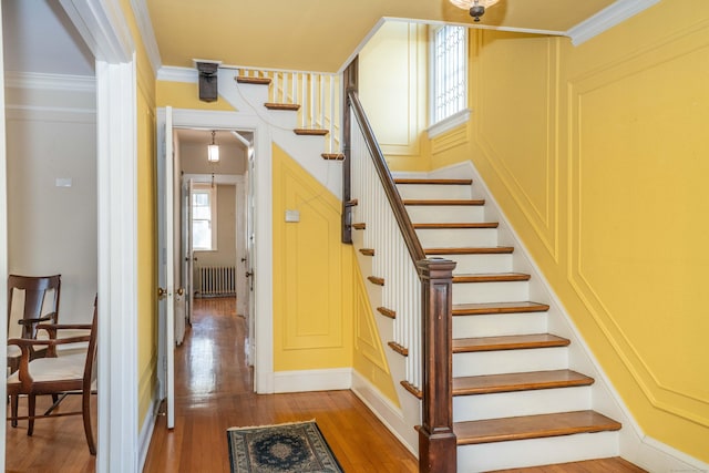 stairs with hardwood / wood-style floors, radiator, and crown molding