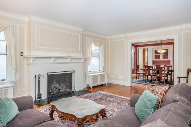 living room featuring a fireplace, light hardwood / wood-style floors, crown molding, and radiator