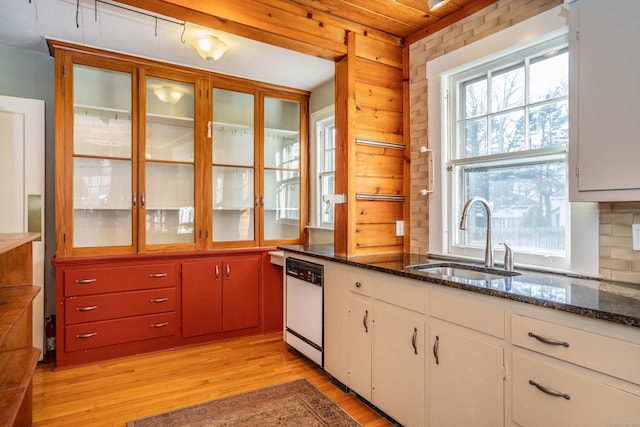 kitchen with light wood-type flooring, dark stone counters, white dishwasher, sink, and white cabinets