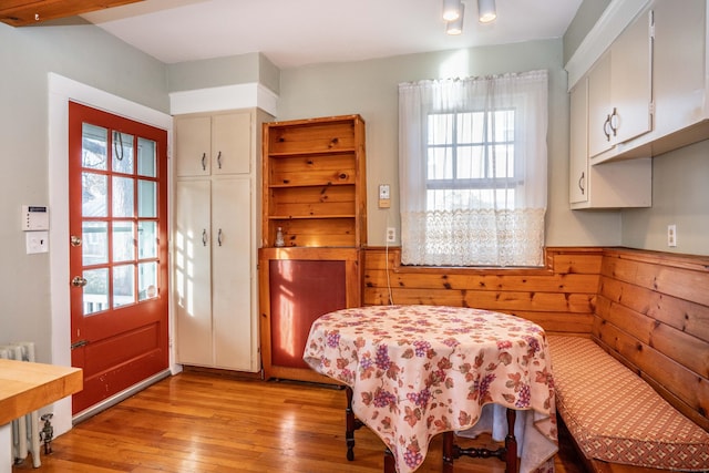 dining room with radiator heating unit, light wood-type flooring, and wooden walls