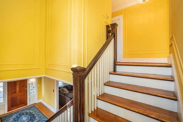 stairs with ornamental molding, a notable chandelier, and wood-type flooring