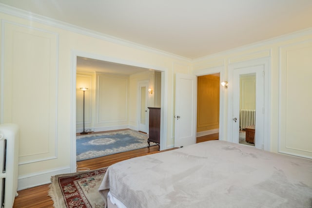 bedroom with radiator heating unit, ornamental molding, and wood-type flooring