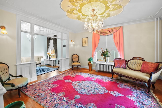 living area with crown molding, radiator, an inviting chandelier, decorative columns, and hardwood / wood-style floors