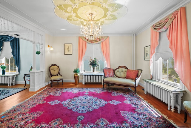 living area featuring radiator, hardwood / wood-style flooring, crown molding, and a chandelier