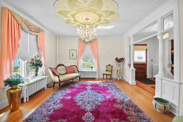 living area with ornamental molding, decorative columns, radiator, and light hardwood / wood-style flooring