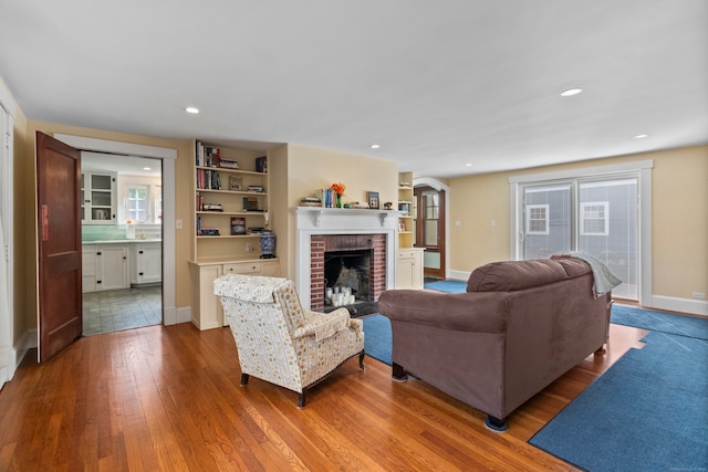 living room with wood-type flooring, a brick fireplace, and built in shelves