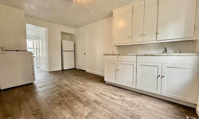 kitchen with white cabinets, a textured ceiling, light wood-type flooring, and white fridge