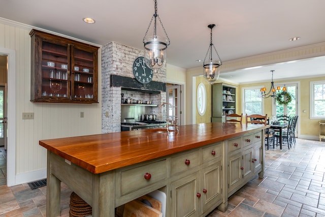 kitchen featuring hanging light fixtures, ornamental molding, sink, wooden counters, and a kitchen island with sink