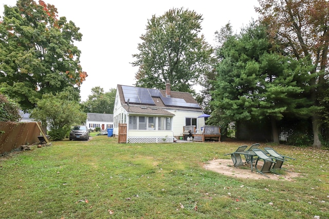 back of property with solar panels, a wooden deck, and a yard