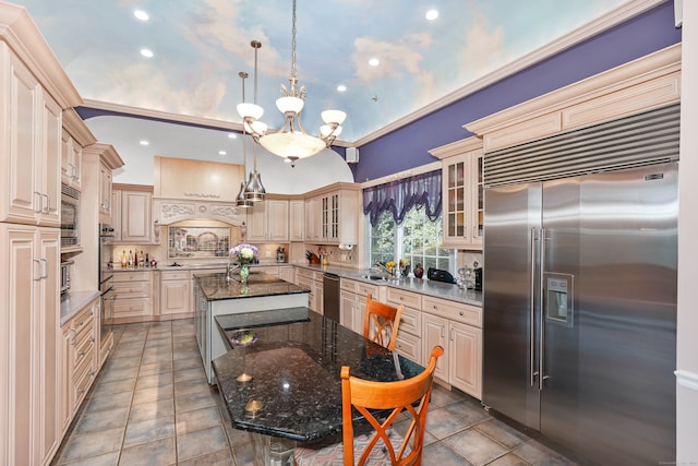 kitchen featuring decorative light fixtures, a center island with sink, built in appliances, dark stone countertops, and a notable chandelier