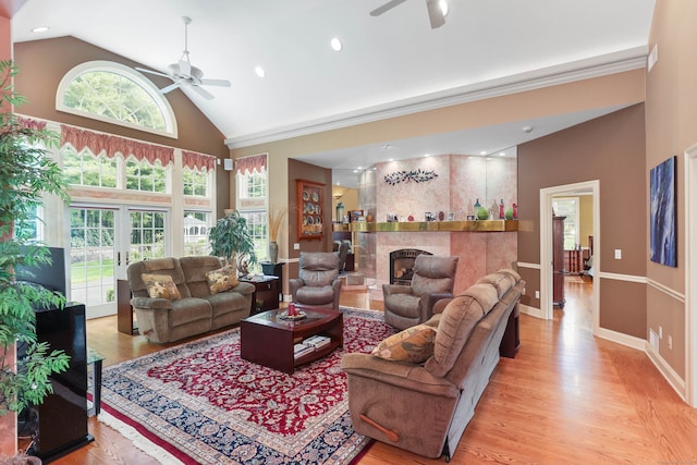 living room featuring light wood-type flooring, a tile fireplace, ceiling fan, and high vaulted ceiling