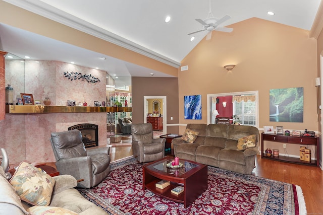 living room with high vaulted ceiling, a tile fireplace, crown molding, ceiling fan, and hardwood / wood-style flooring