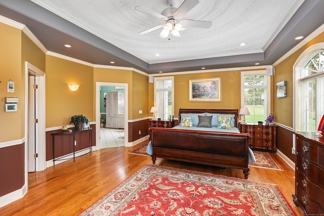 bedroom featuring light hardwood / wood-style flooring, a tray ceiling, ceiling fan, and ornamental molding