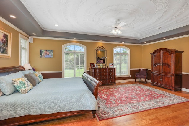 bedroom featuring ceiling fan, a raised ceiling, ornamental molding, hardwood / wood-style flooring, and access to exterior