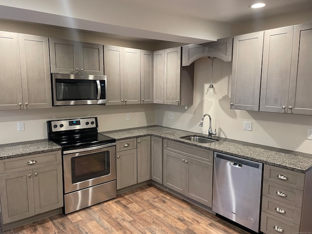 kitchen with sink, light hardwood / wood-style flooring, gray cabinets, appliances with stainless steel finishes, and dark stone counters