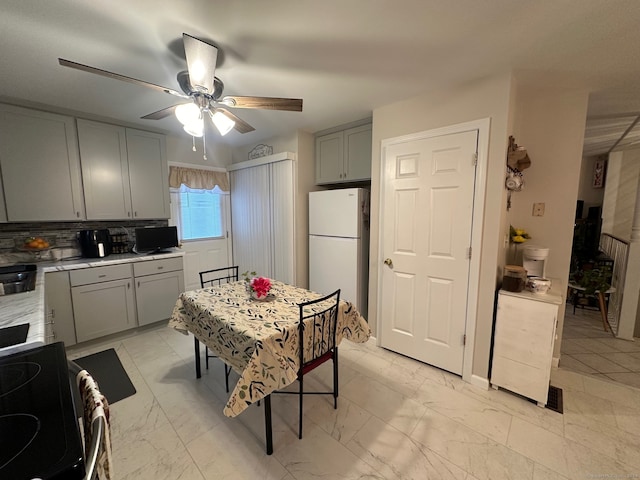 kitchen with gray cabinetry, ceiling fan, range, decorative backsplash, and white fridge