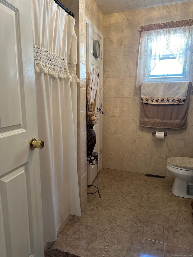 bathroom featuring tile walls, tile patterned floors, and toilet