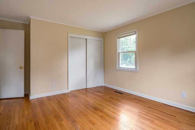 unfurnished bedroom with a closet, crown molding, and light wood-type flooring