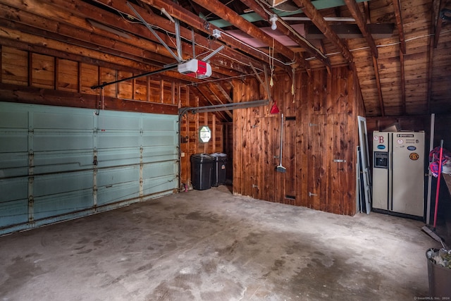 garage featuring a garage door opener, stainless steel fridge with ice dispenser, and wooden walls